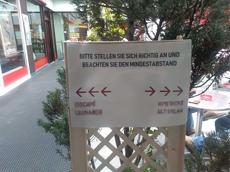 Zwei nebeneinanderliegende Geschäfte definieren mit Hinweisschildern Zugänge, um den Kundenstrom zu regeln und einen geordneten Zugang zu ermöglichen.
